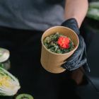 A hand holding a salad bowl with fresh vegetables and a colorful garnish, emphasizing healthy eating.