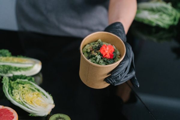 A hand holding a salad bowl with fresh vegetables and a colorful garnish, emphasizing healthy eating.