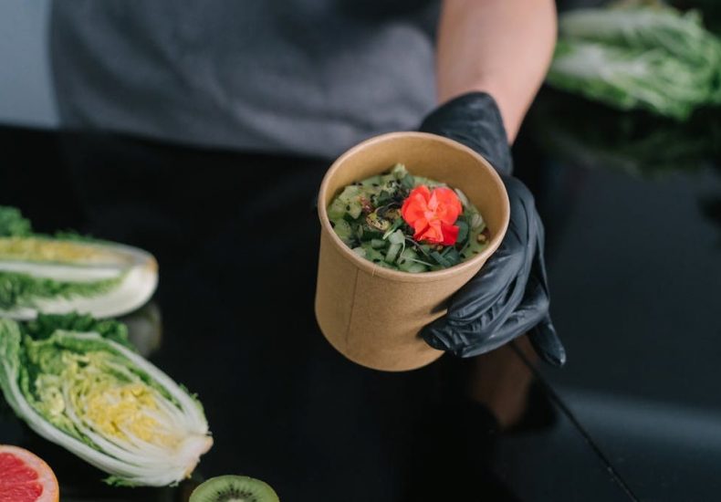A hand holding a salad bowl with fresh vegetables and a colorful garnish, emphasizing healthy eating.